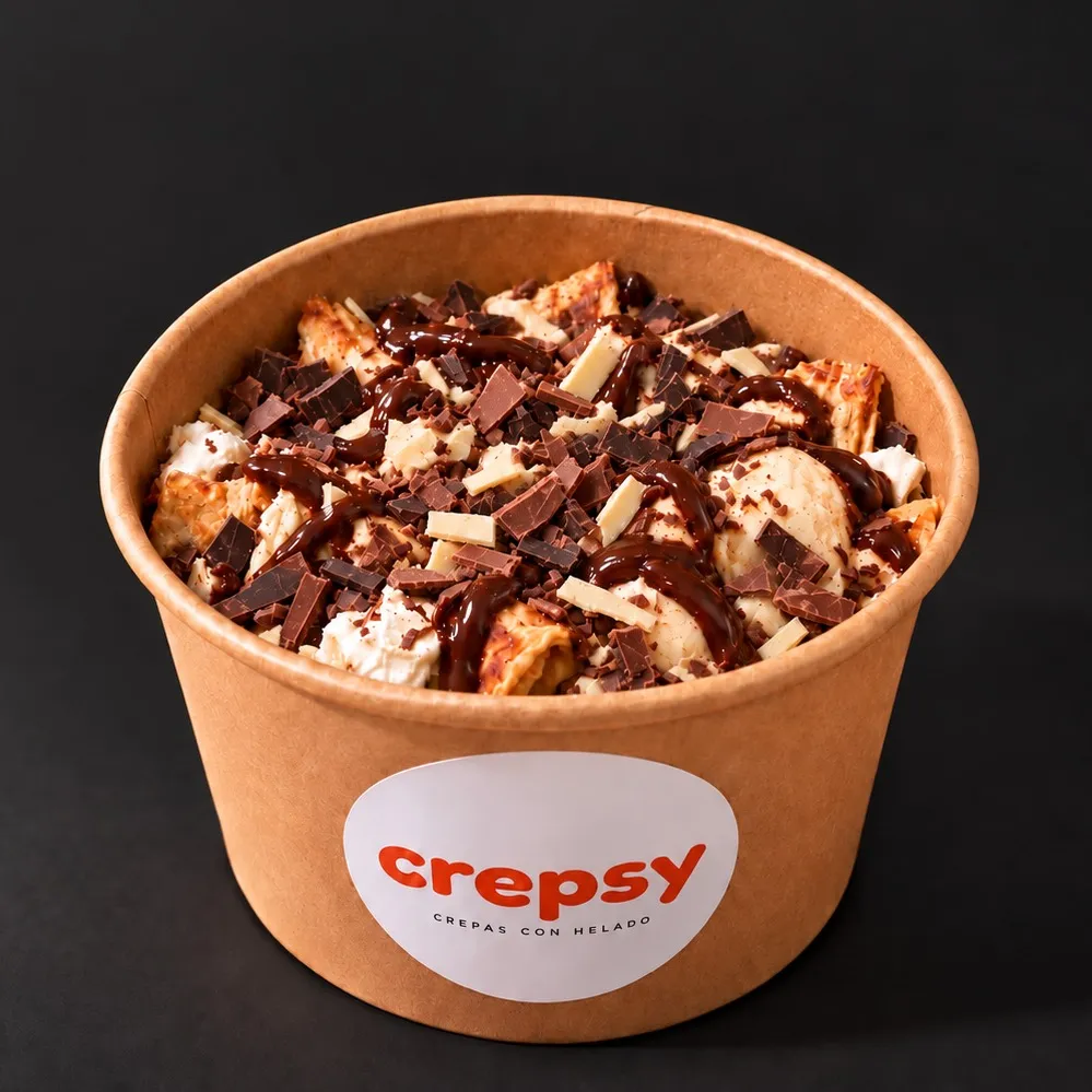 Bowl de papel con crepa y helado cubiertos de trozos de chocolate oscuro, con leche y blanco y salsa de chocolate