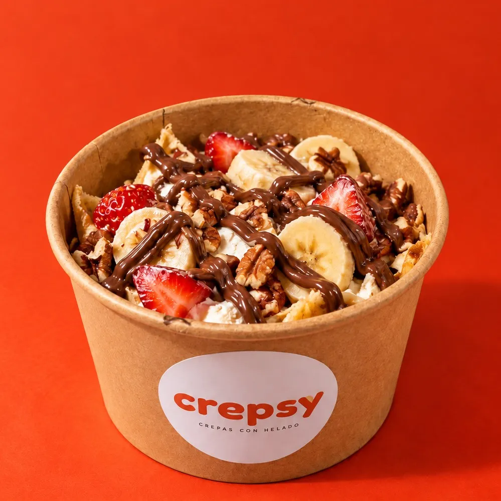 Bowl de papel con crepa y helado, fresa, plátano en rodajas, nuez pecana y Nutella en hilos